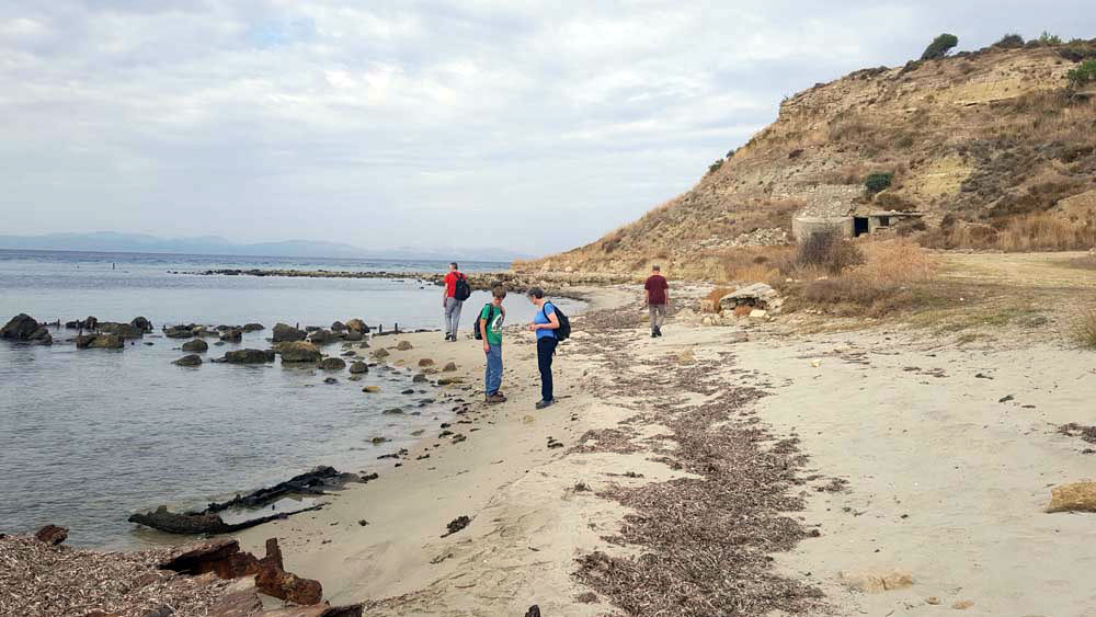 Several people standing or walking on a small sandy beach.