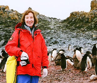 A white woman wearing a red windbreaker jacket posing with penguins