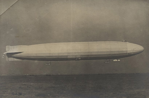 Black and white photograph. Side view of a very long zeppelin in the air