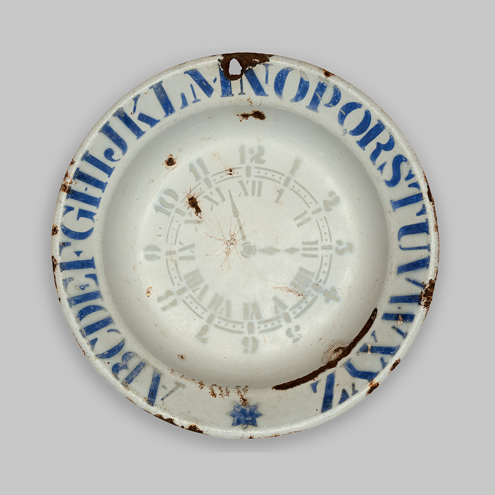Photographie moderne d'une assiette avec des lettres latines peintes sur le pourtour.