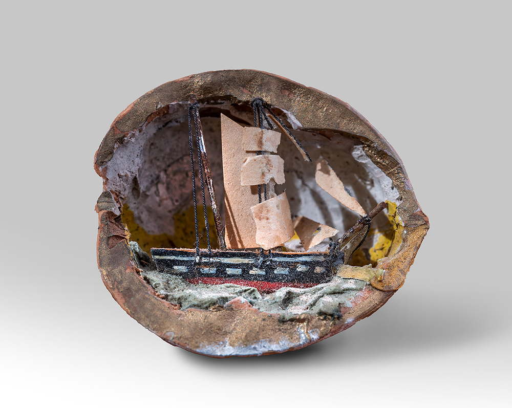 Modern photograph of a handcarved walnut shell diorama depicting a sailing vessel on the waves