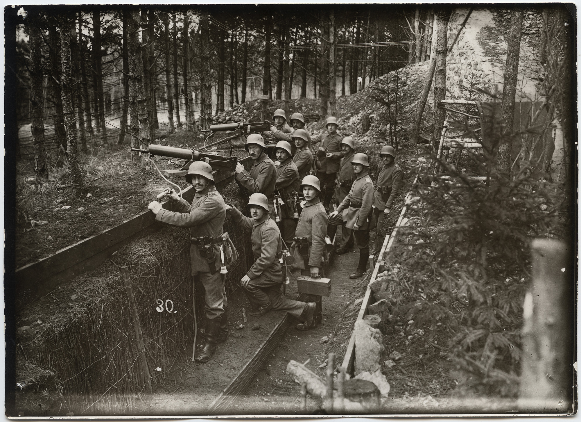 Black and white photograph of a group of men in WWI uniform standing and sitting in a trench looking up at the viewer