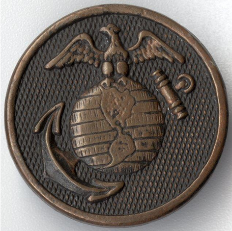 Photograph of a bronze-colored lapel pin engraved with the U.S. Marines logo: an eagle astride a globe over an anchor