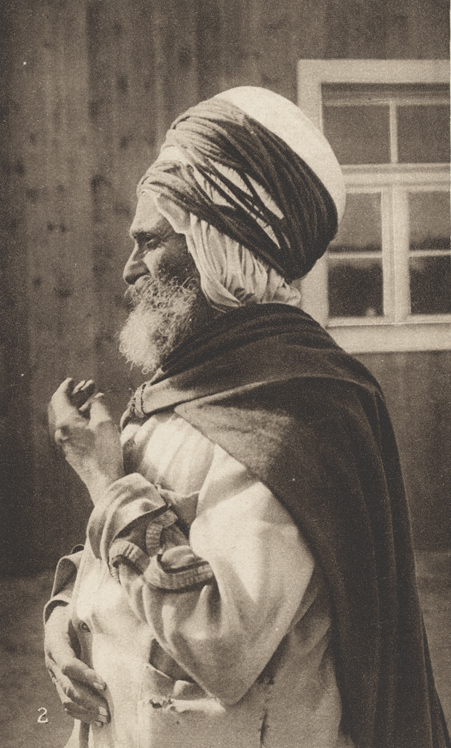 Photographie sépia d'un homme barbu portant des robes amples, un manteau et un turban
