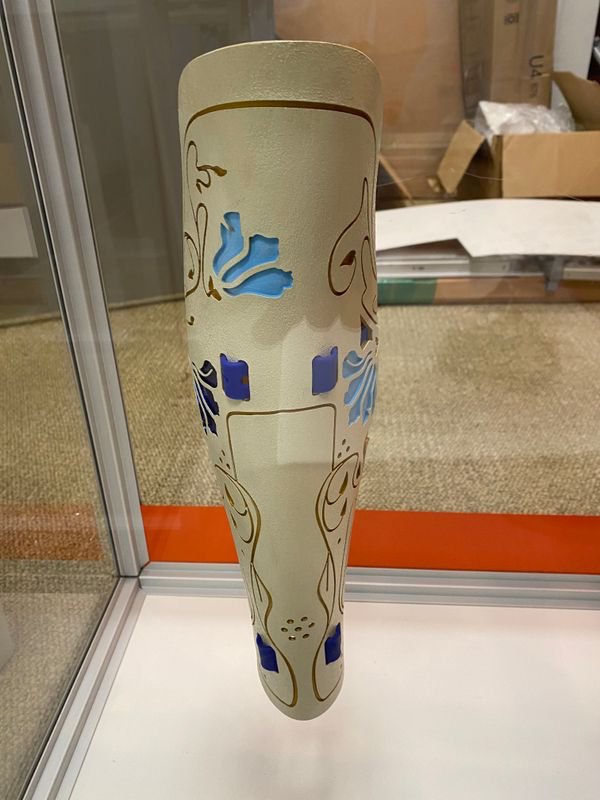 Modern photograph of a modern-day cover for a prosthetic leg - an ivory color with art noveau floral designs in blue and gold