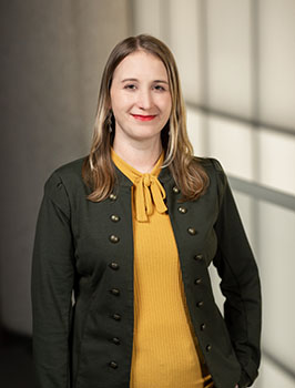 Headshot of a young white woman with shoulder-length light brown hair, wearing a dark jacket and yellow shirt