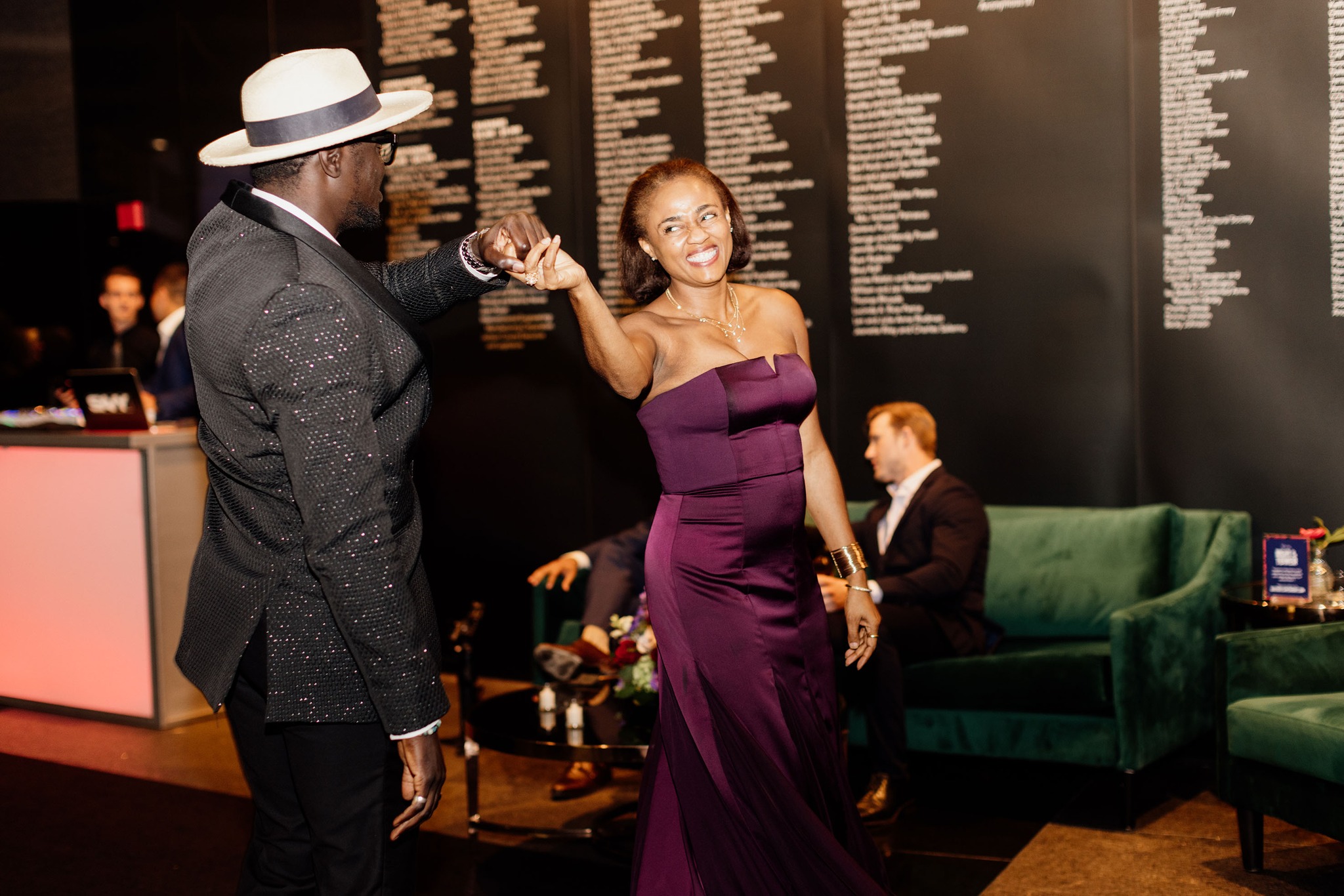 Modern photograph of a Black man in a suit and white brimmed hat twirling a Black woman in a purple satin evening gown