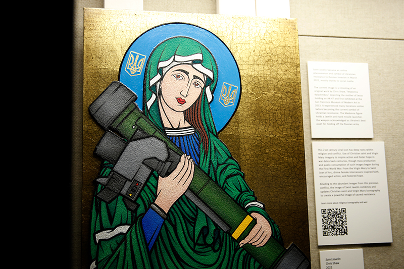 Modern photograph of the Saint Javelin physical painting displayed in a glass case next to labels filled with text.