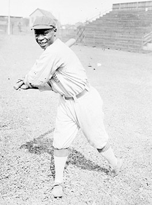 Black and white photo of a black man wearing a baseball uniform swinging a bat