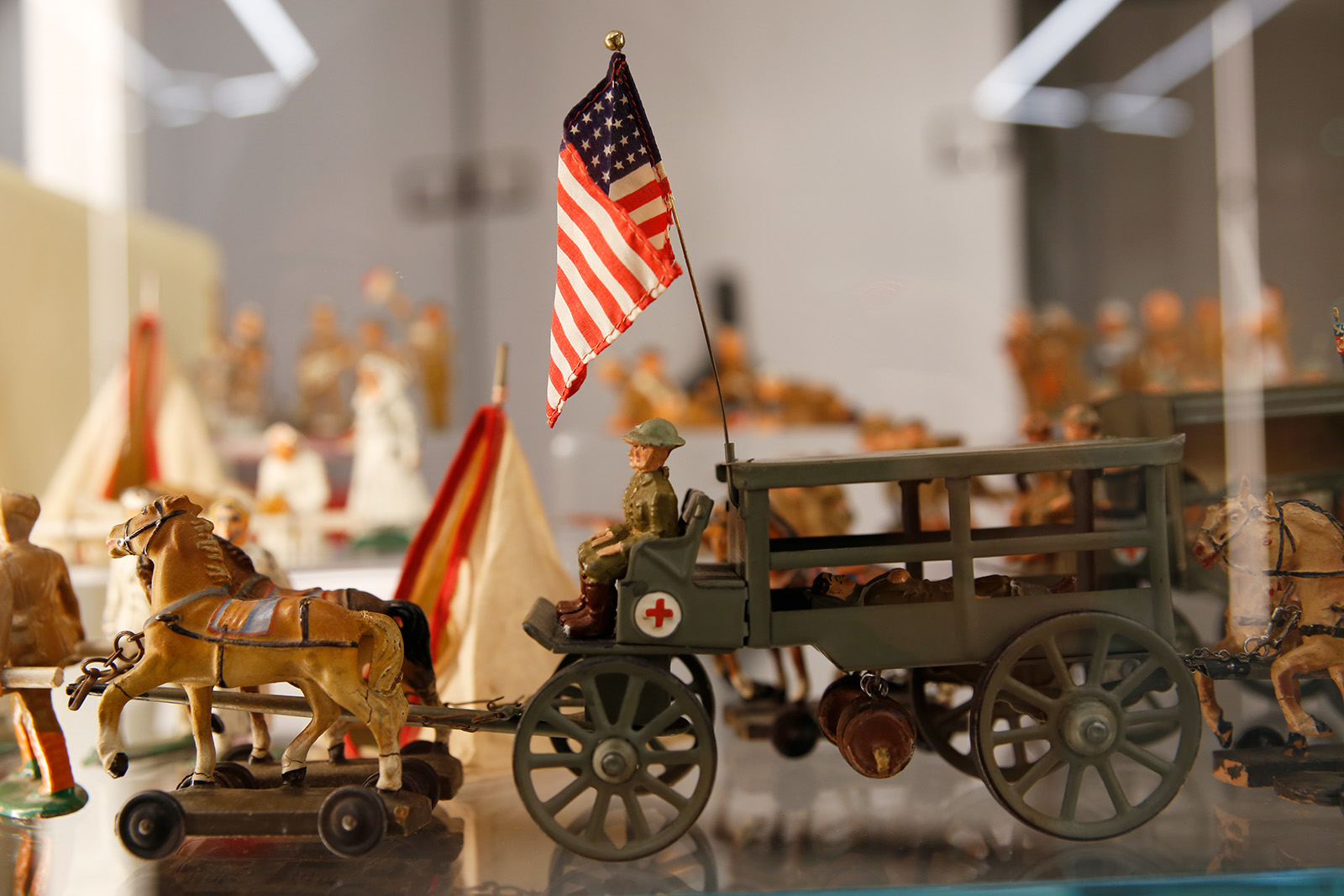 Modern photograph of a glass display case featuring a small toy ambulance drawn by toy horses