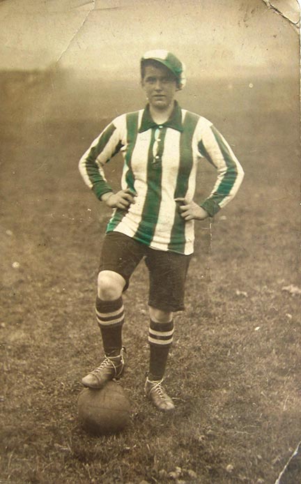 Sepia photograph of a woman wearing a green- and white-striped jersey, with one foot up on a soccer ball.