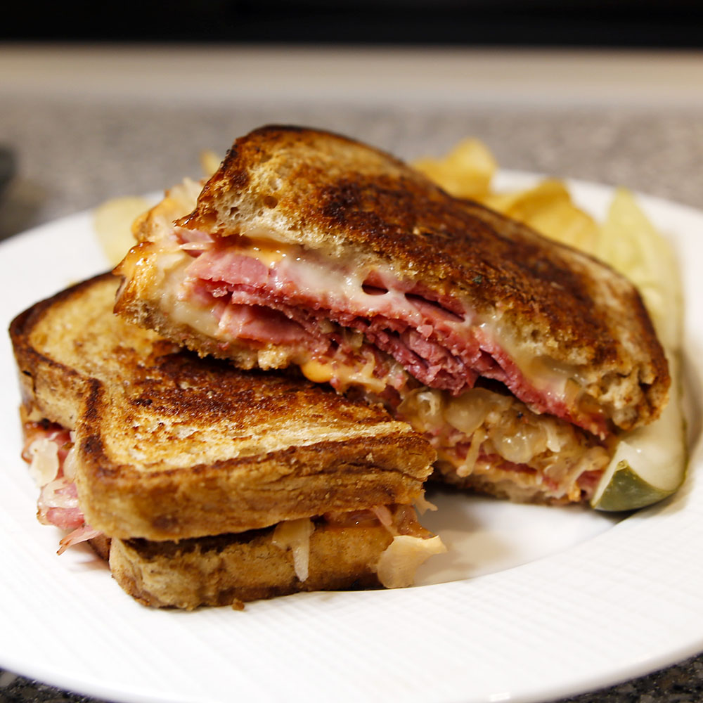 Modern photograph of a reuben sandwich sliced in two.