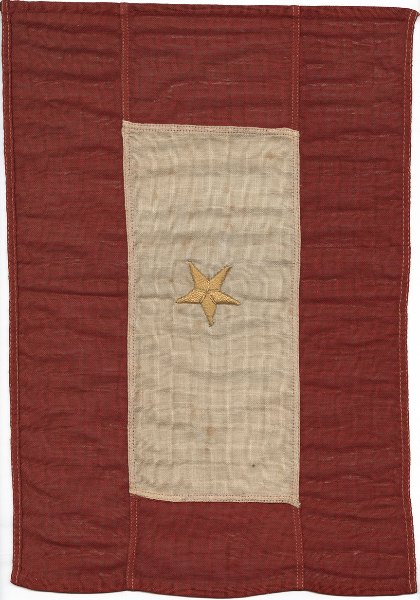 Modern photograph of a WWI-era flag. A red border surrounds a cream/white rectangle. A single gold star is embroidered in the center.