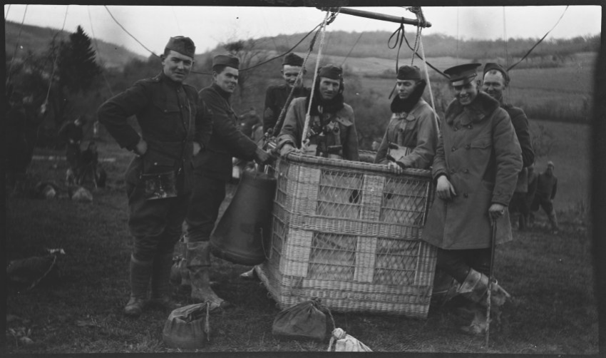 Black and white photograph of a WWI balloon basket tethered to the ground with two balloon pilots in the basket.