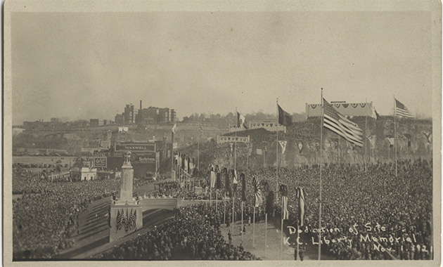 Black and white vintage photograph of massive crowds gathered around a large stone platform on a hill with flags flying everywhere.
