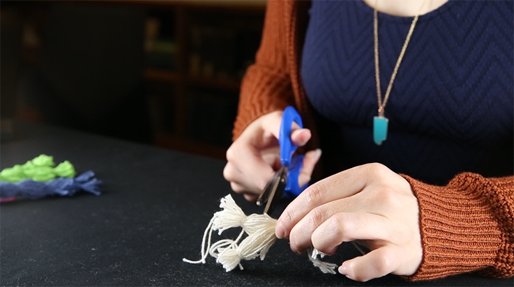 A person cutting some of the yarn in the doll's legs