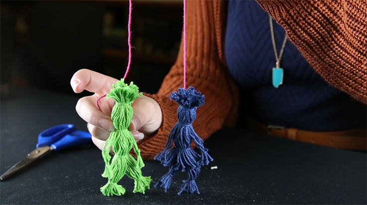 A person showing a completed green Rintintin doll and a completed blue Nenette doll connected by a pink string