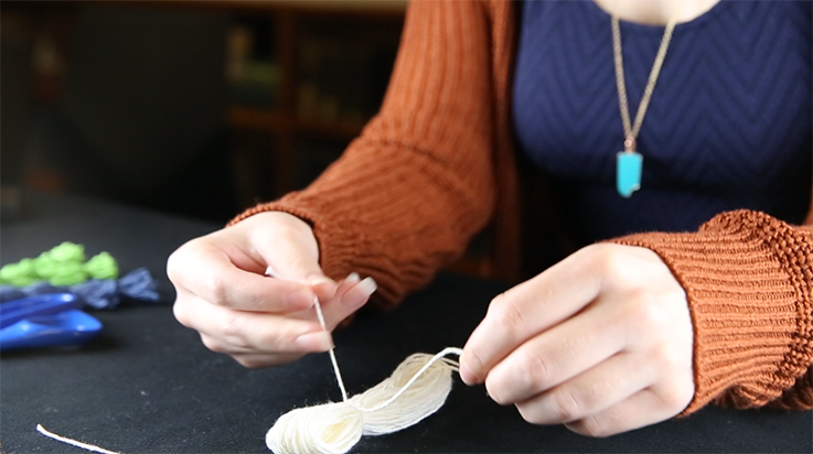 A person tying a piece of yarn around the looped bundle (side view)