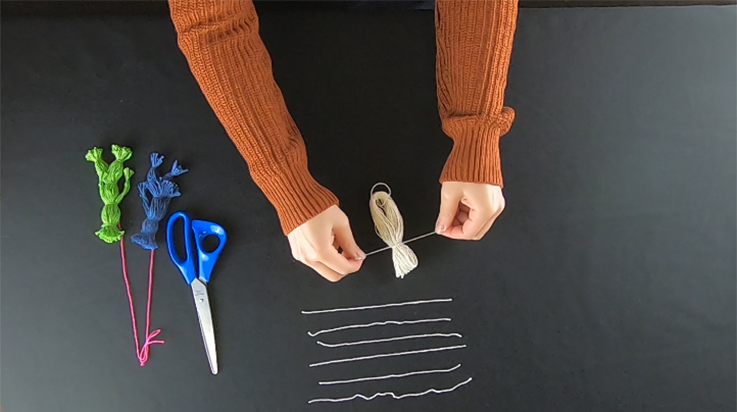 A person tying a piece of yarn around the looped bundle (top view)