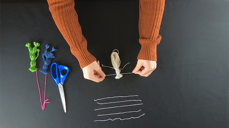 A person tying a second piece of yarn closer to the top of the bundle of looped yarn (top view)