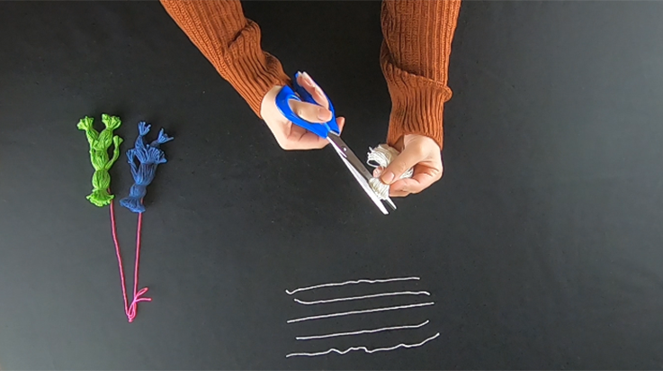 A person cutting the top of the looped bundle of yarn