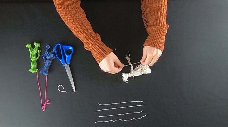 A person tying a piece of yarn around several strands separated from the main bundle