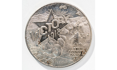 Modern photograph of a silver coin engraved with clouds, the sun and a large star. Engraved text: 'Victory 1918'