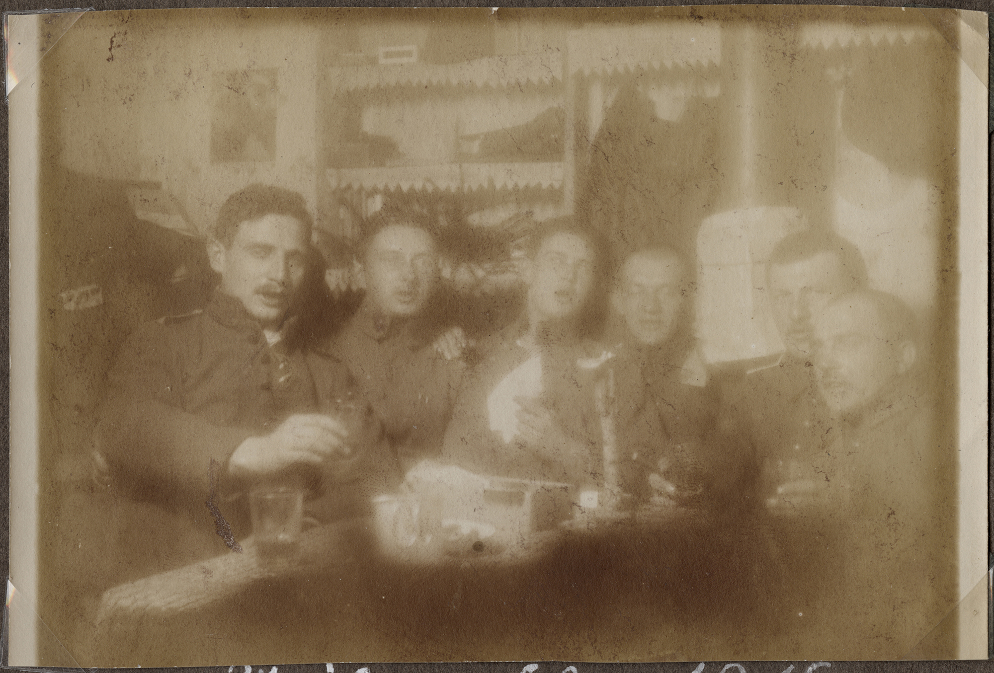 Fuzzy sepia picture of a group of soldiers seated around a table scattered with drinks and toasting the camera