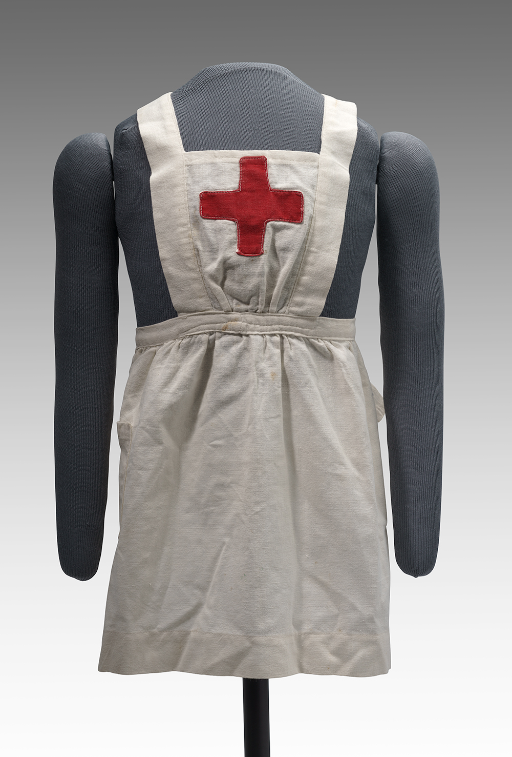 Modern photograph of a small white smock apron with a red cross on the front