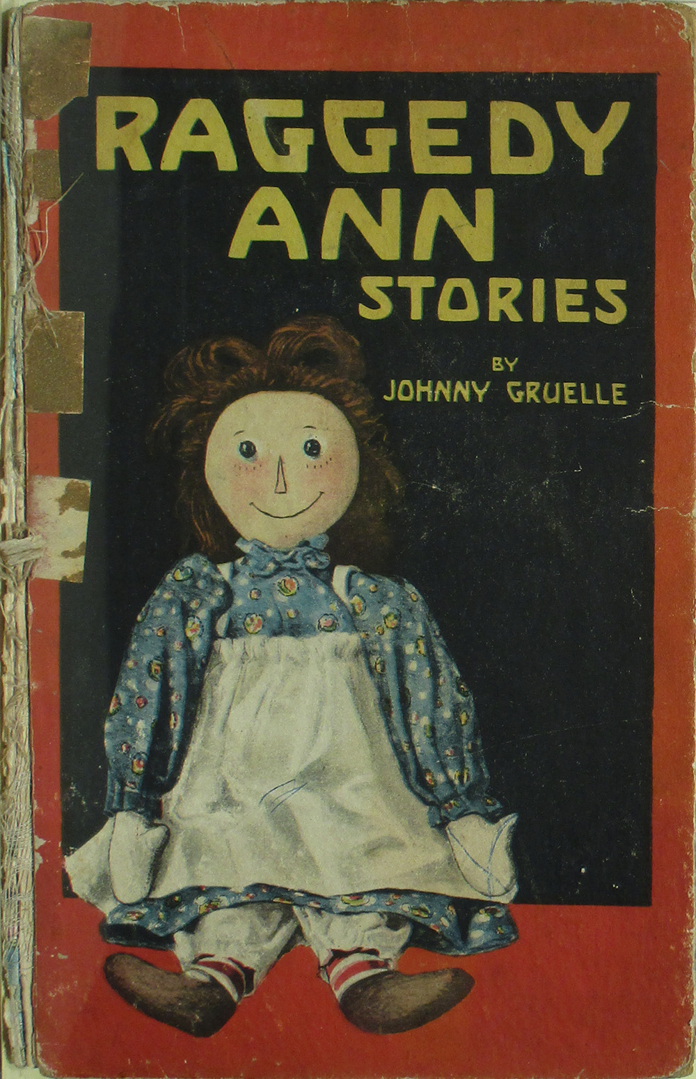 Ancienne couverture de livre en lambeaux illustrant une poupée de chiffon souriante portant une robe bleue et un tablier blanc. Texte : « Histoires de Raggedy Ann »