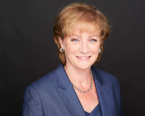 Modern headshot of a middle-aged white woman with short auburn/brown hair wearing a blue suit jacket