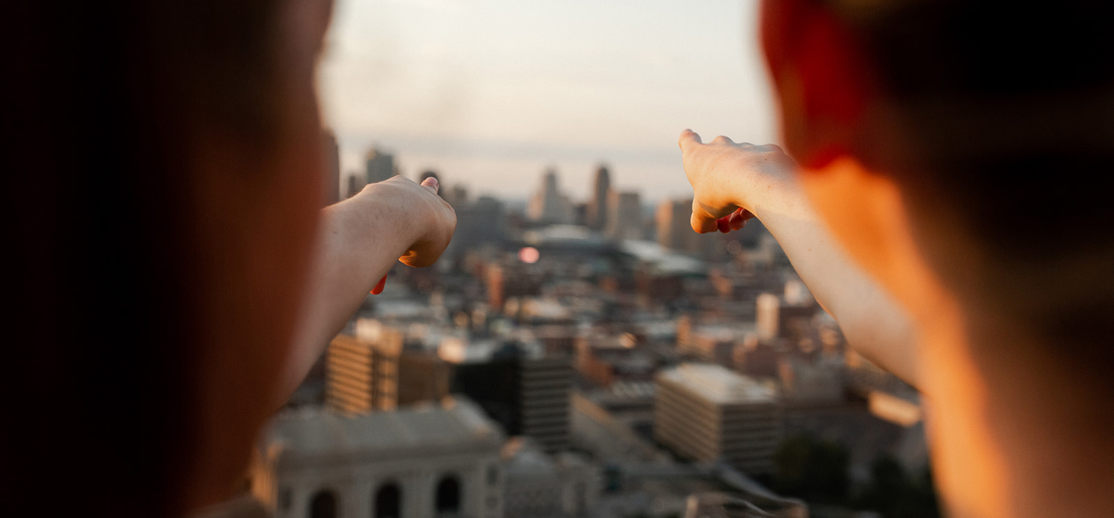 Modern photograph showing the Kansas City skyline from the point of view of two people on top of the Liberty Memorial Tower. Both are pointing at something on the horizon.