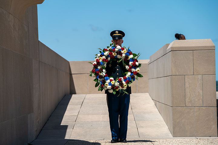 Modern photograph of a person in military uniform standing on Memorial Courtyard holding a large memorial wreath
