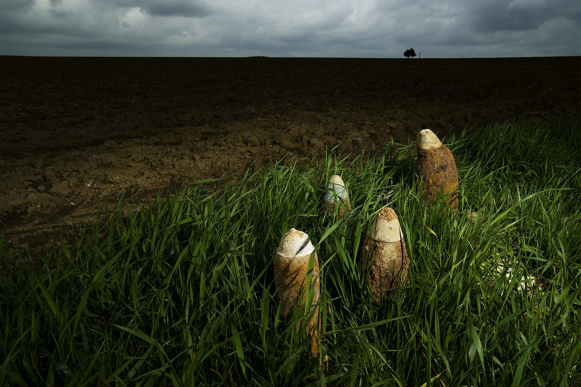 Modern photograph of four unexploded shells sitting in the grass next to a plowed field
