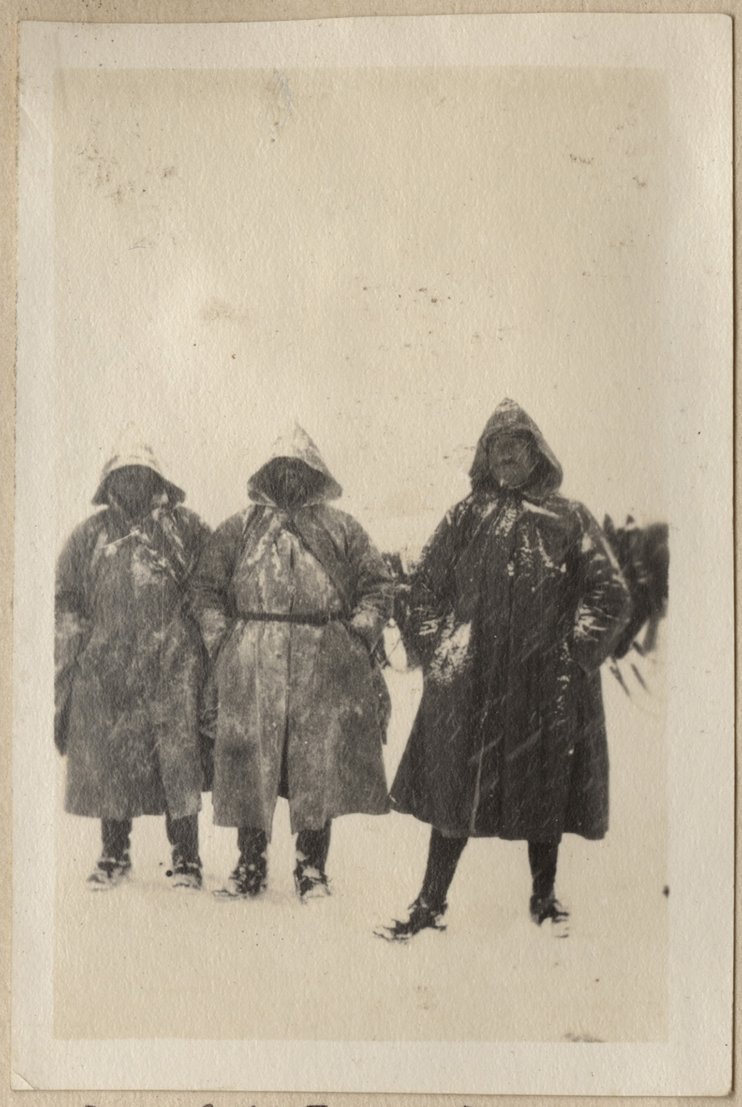 Photographie en noir et blanc de trois hommes portant de lourds manteaux et capuches, debout dans la neige