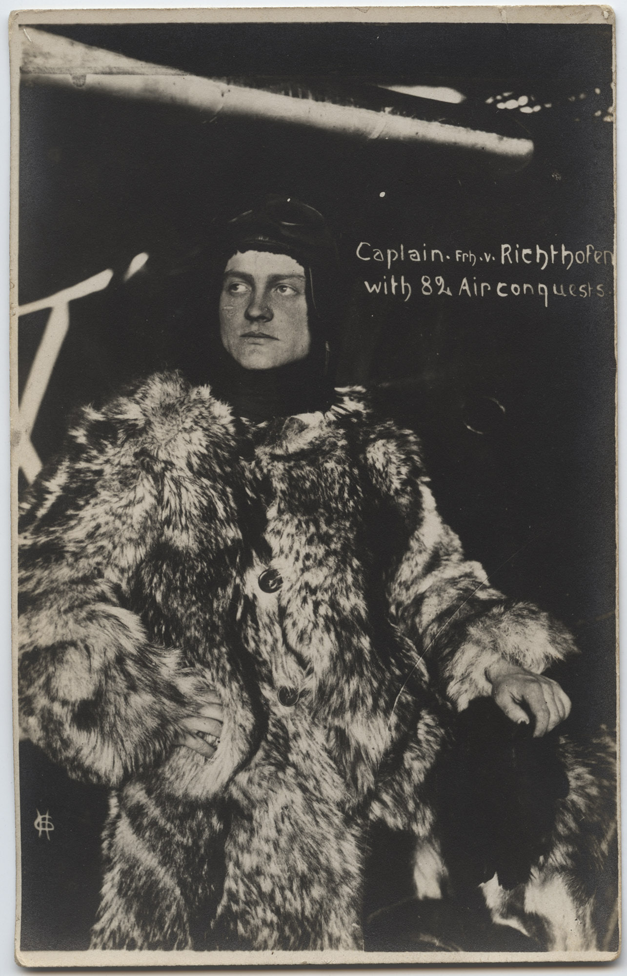 Photographie de portrait en noir et blanc d'un jeune homme blanc posant dans un grand manteau de fourrure et une casquette d'aviateur en cuir