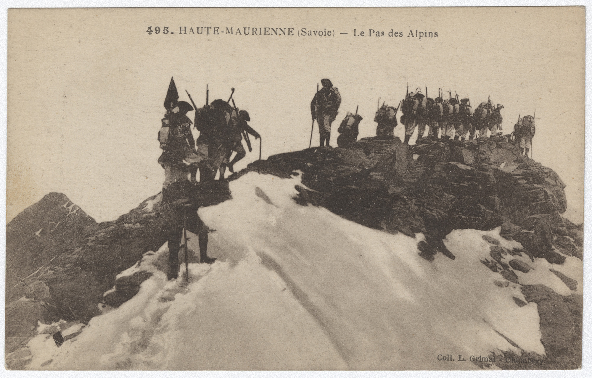 Photographie en noir et blanc d'une ligne de soldats chargés de sacs et d'armes marchant péniblement sur une crête de montagne