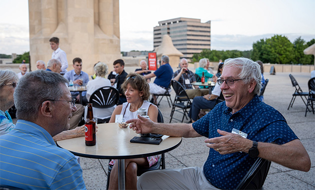 Groups of people chatting and laughing around cocktail tables on Memorial Courtyard with the Liberty Memorial Tower in the background.