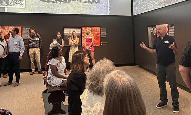 A group of people in a museum gallery listening to a curator speaking