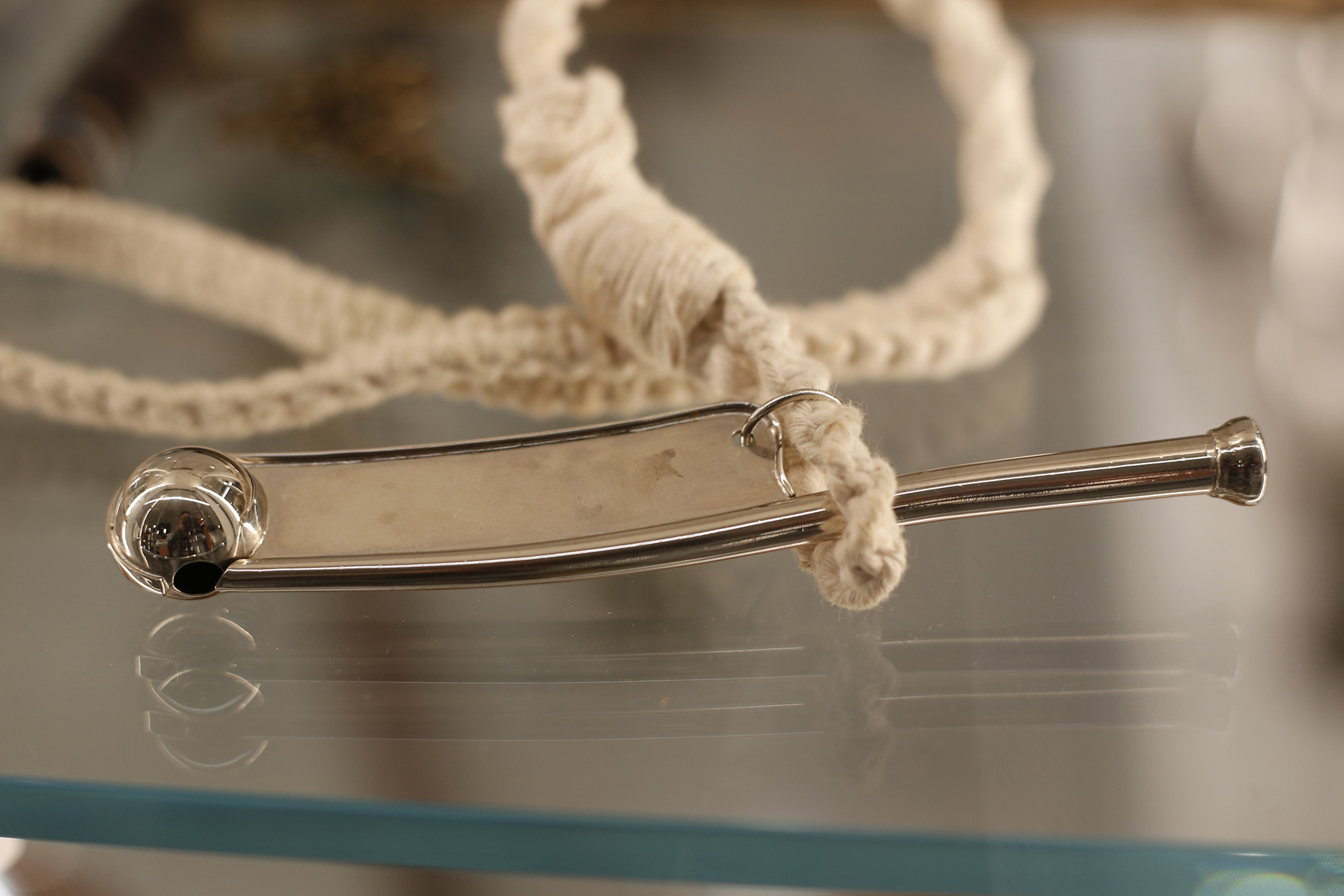 Sifflet en métal argenté composé d'un tuyau fin avec une pièce plate attachée en dessous et une boule attachée à l'extrémité