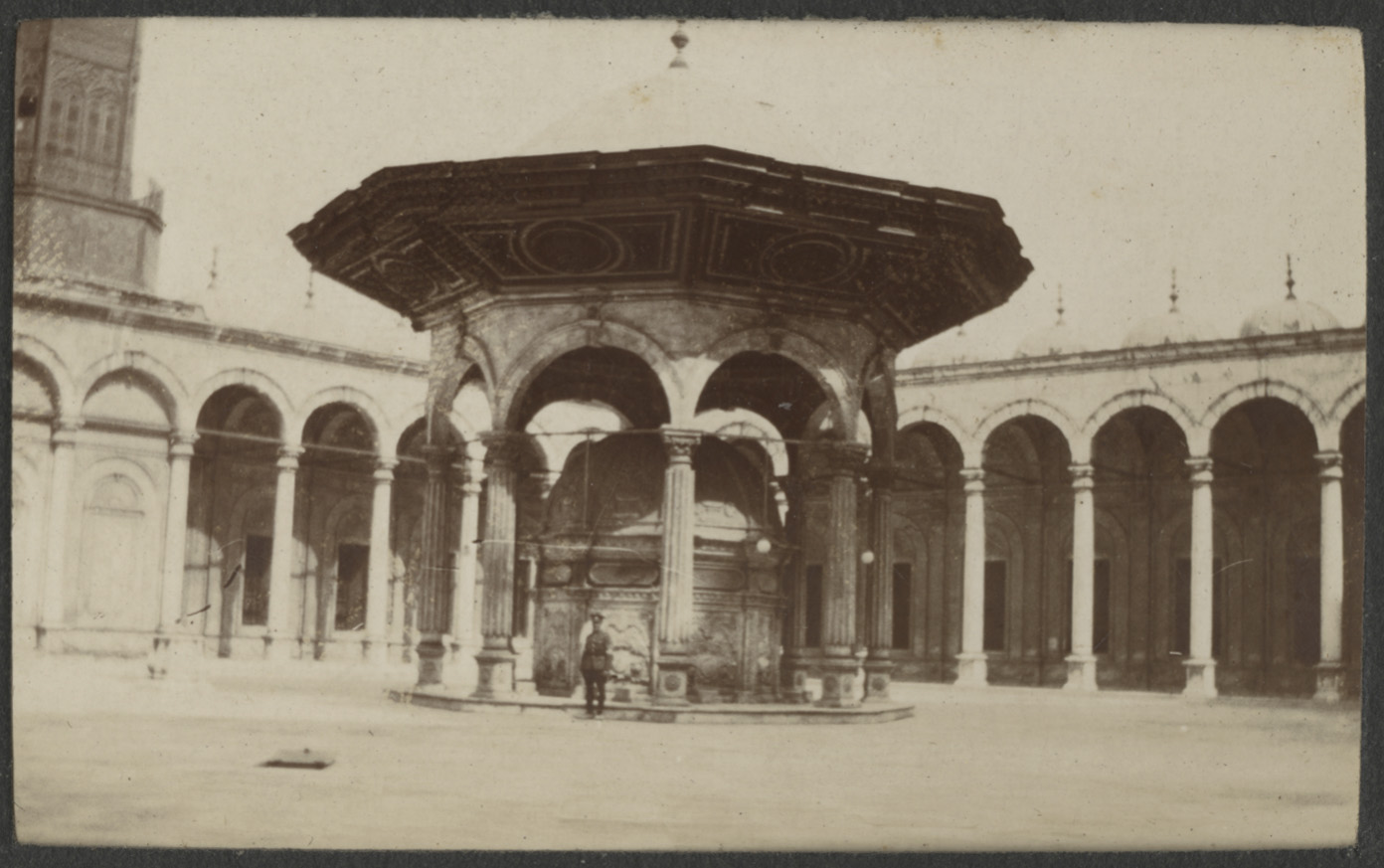 Black and white photograph of a British soldier in uniform standing under a pavilion in a courtyard
