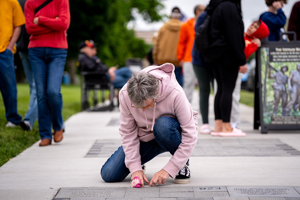 Person wearing a pink sweatshirt and jeans kneeling by a display of engraved bricks embedded in a sidewalk