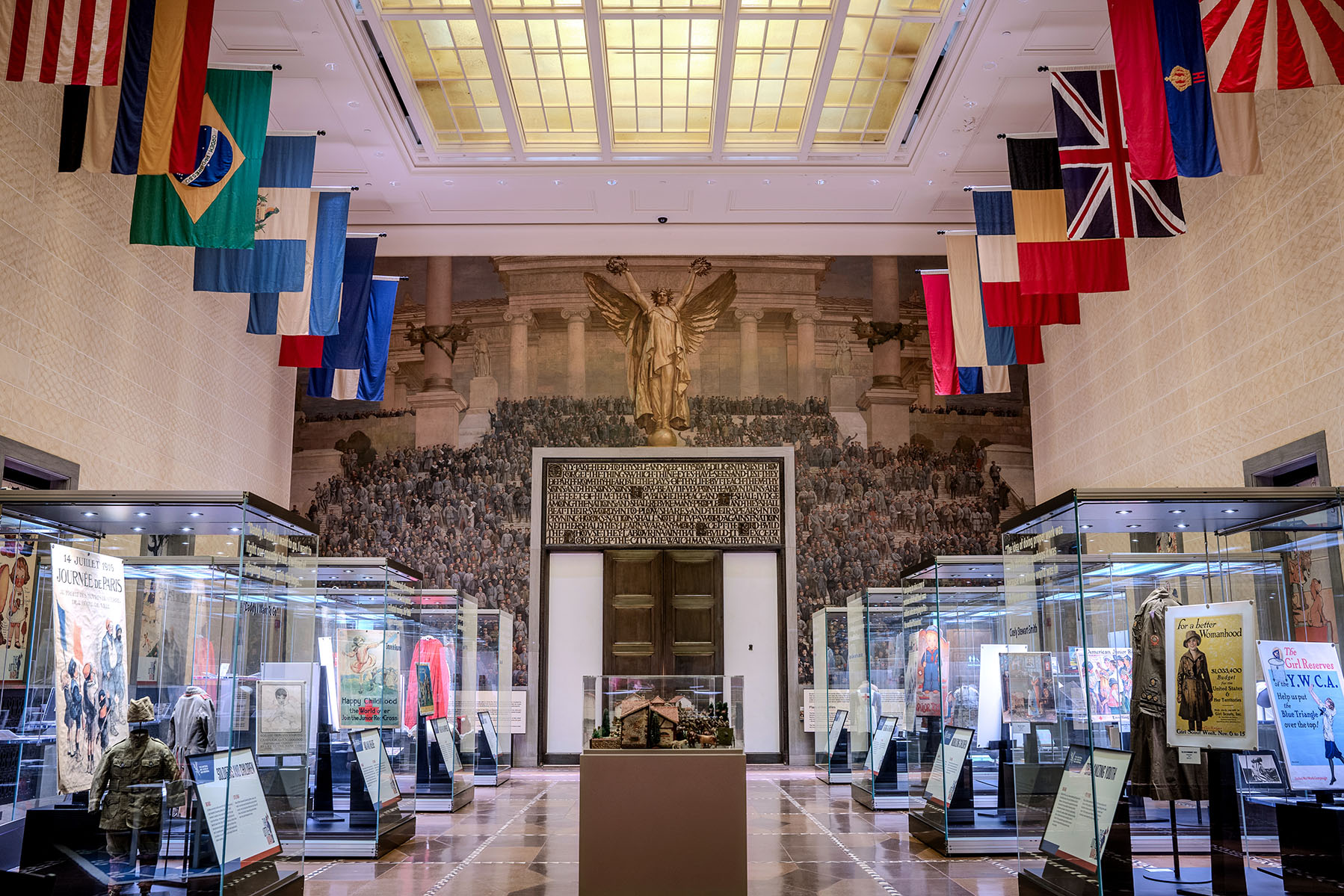 Exhibition hall with a large painting on one end, national flags hanging from the ceiling and glass exhibit cases lining the floor