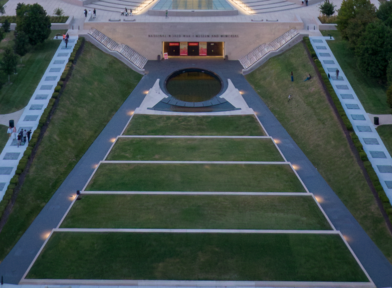 Top-down aerial view of a grassy terraced area leading to an oval pool and the front entrance of the Museum and Memorial