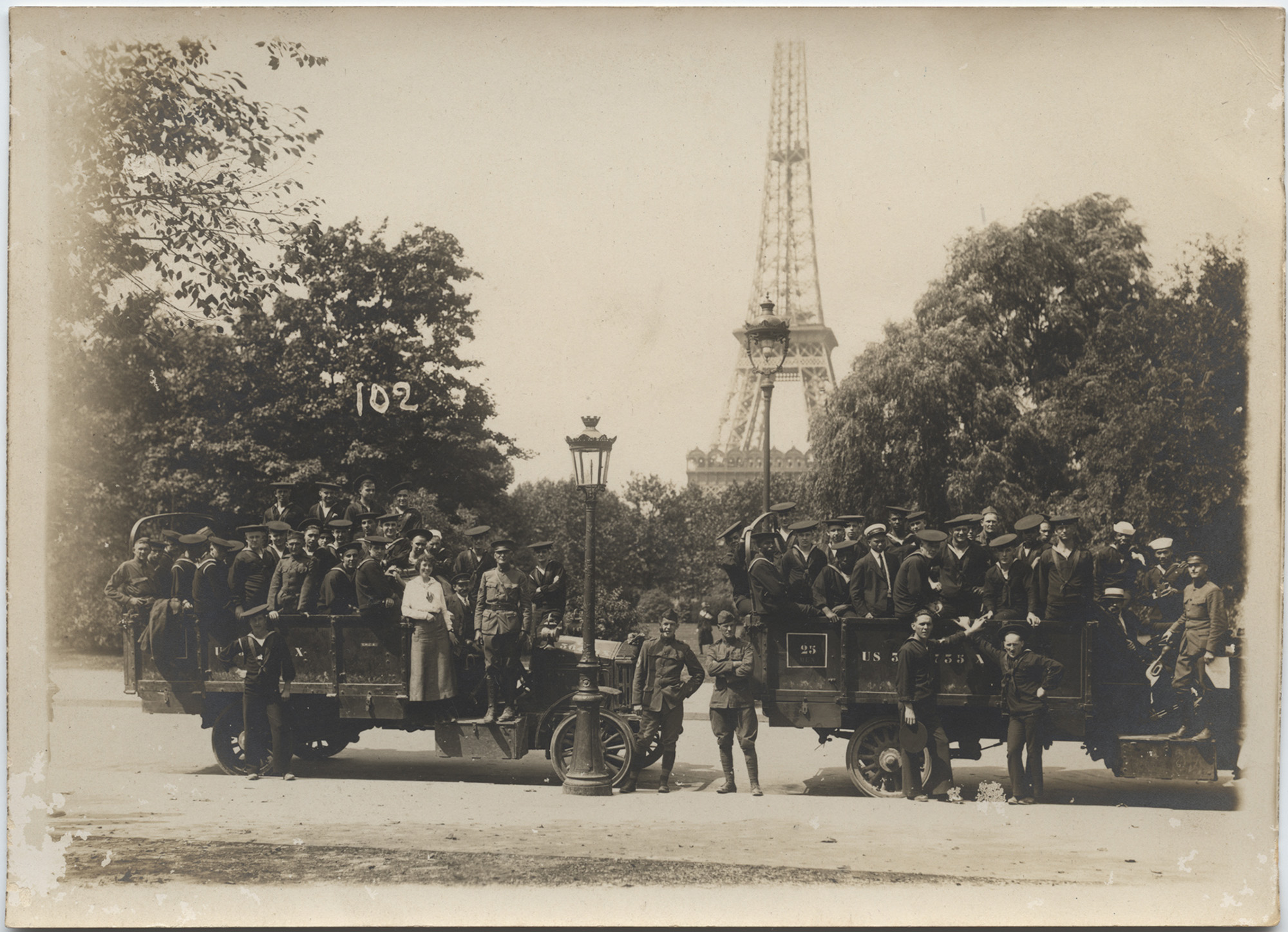 Black and white photograph of two WWI trucks full of soldiers parked in front of the Eiffel Tower