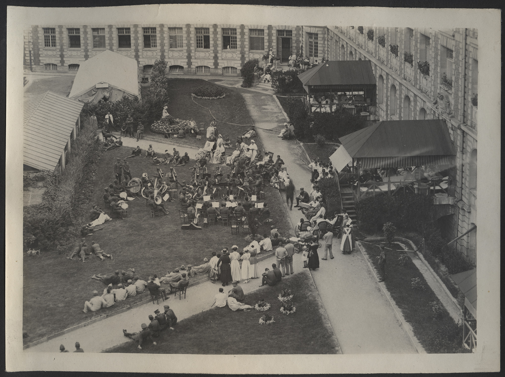 Aerial view of a large courtyard in which people are standing and listening to a band performing on the lawn