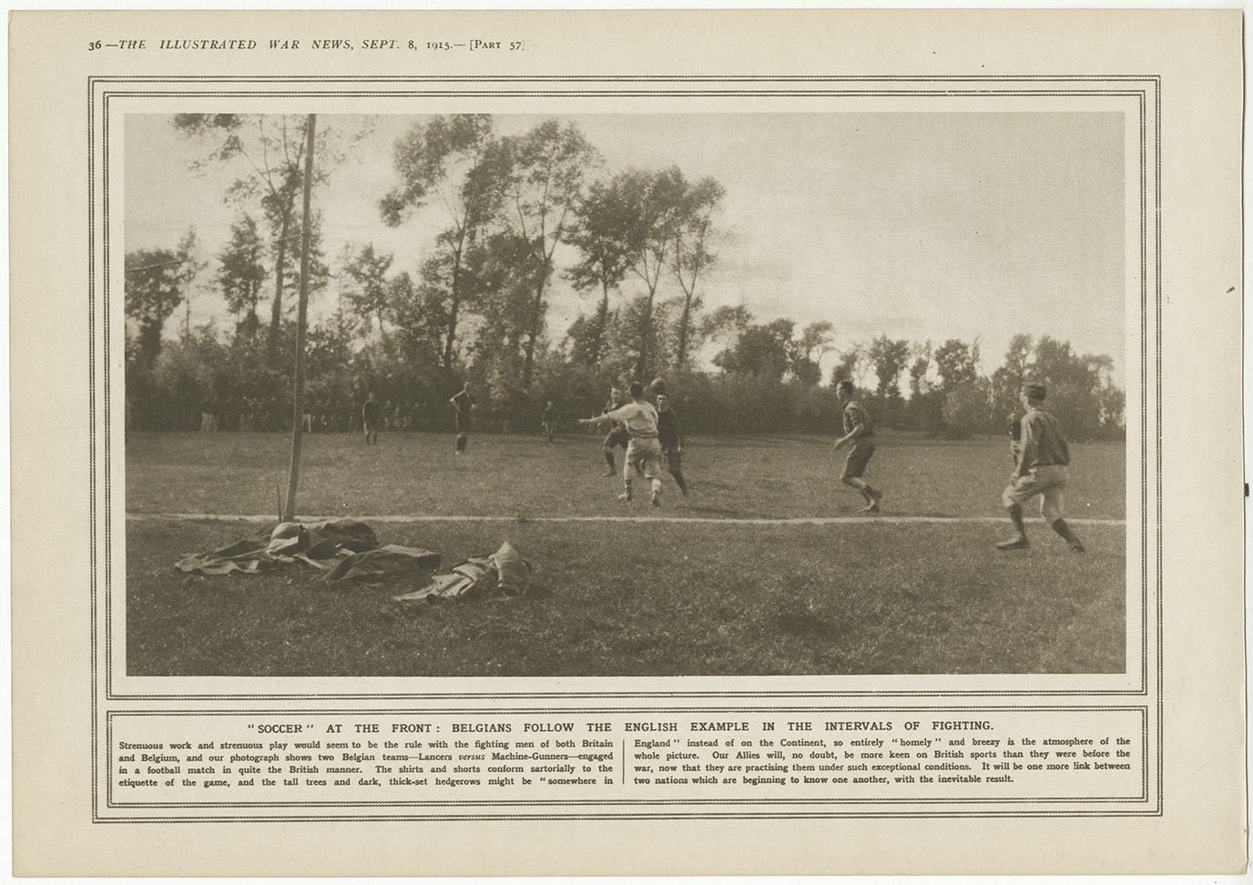 Black and white photo of WWI soldiers stripped down to shirtsleeves playing a game of football in a field surrounded by trees. Abandoned clothes and equipment lie nearby under a tree.