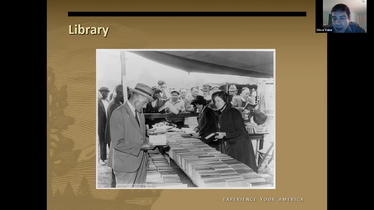 Photographie en noir et blanc de personnes rassemblées autour d'une longue table chargée de livres