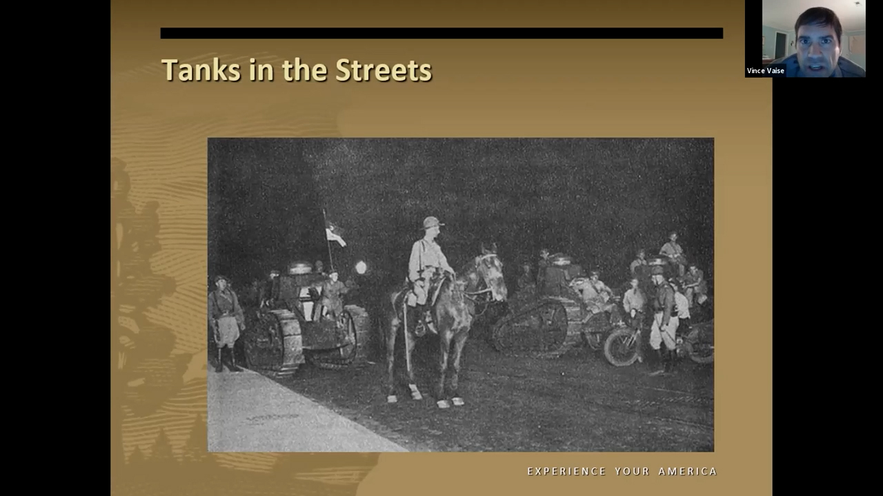 Photo en noir et blanc de soldats à cheval au milieu de très petits chars de la Première Guerre mondiale roulant dans la rue
