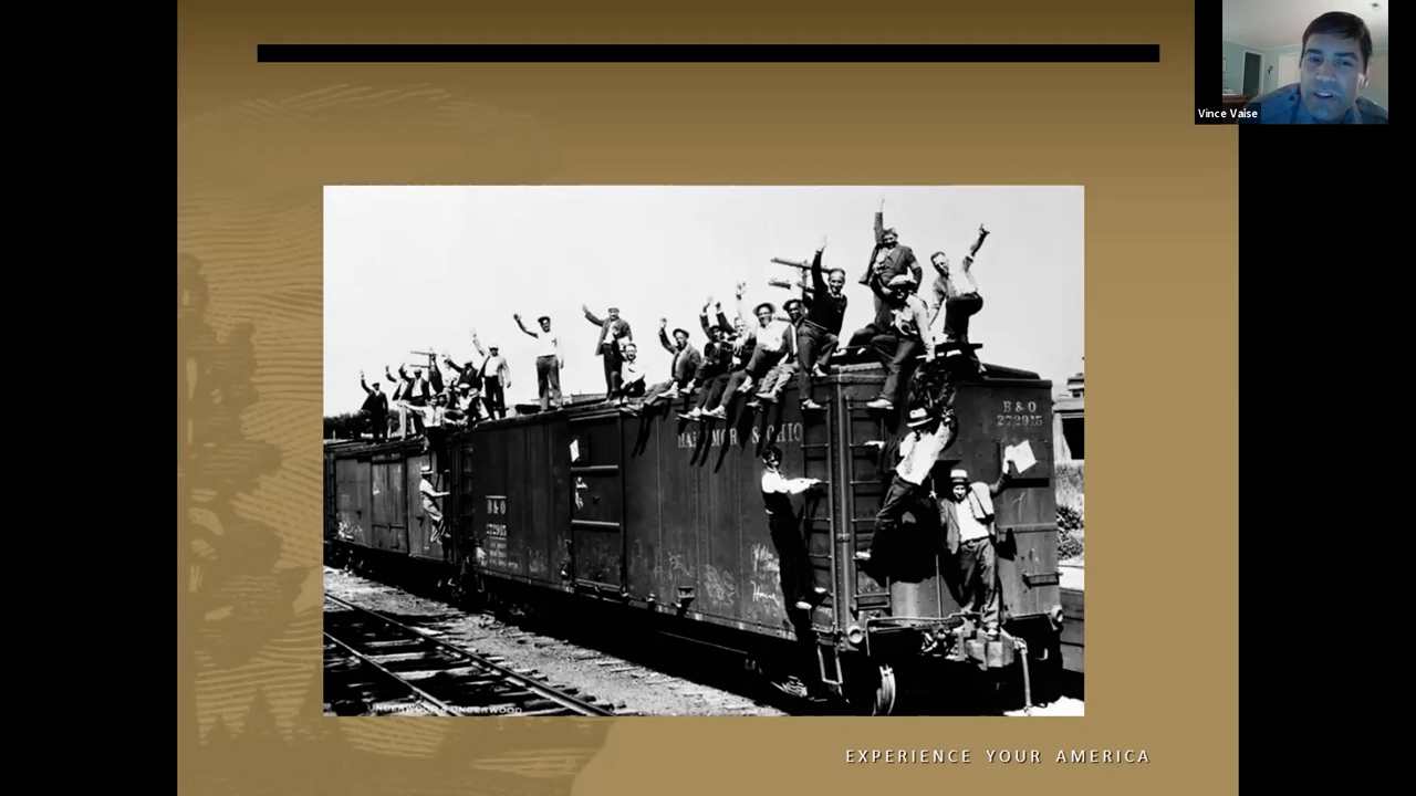 Photographie en noir et blanc d'un wagon couvert d'hommes debout sur le toit et accrochés aux côtés